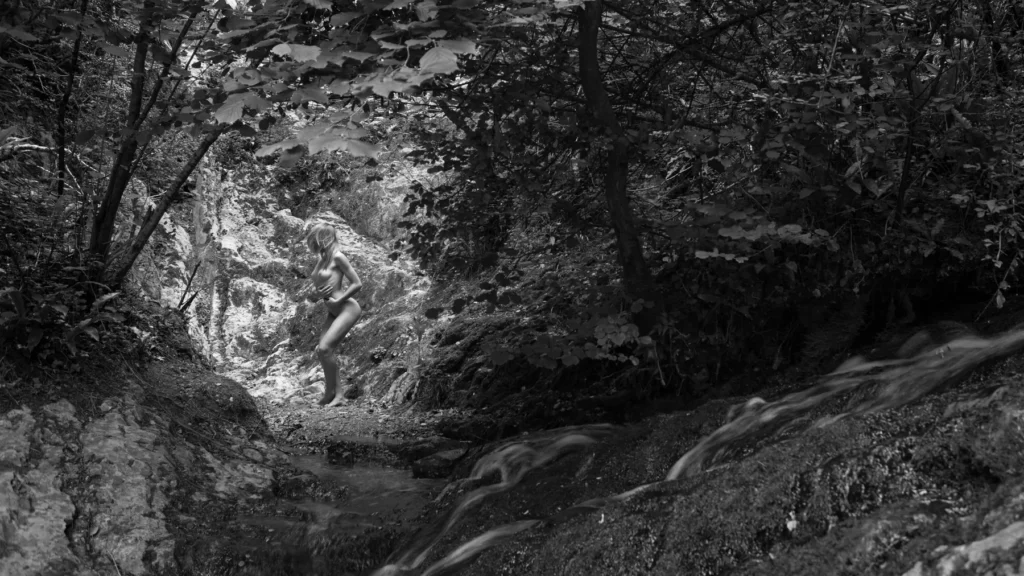 Nu artistique en noir et blanc intégré à un paysage de forêt et de ruisseau.